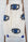 White blanket with black and blue evil eye patterns draped over a wooden ladder against a white brick wall.