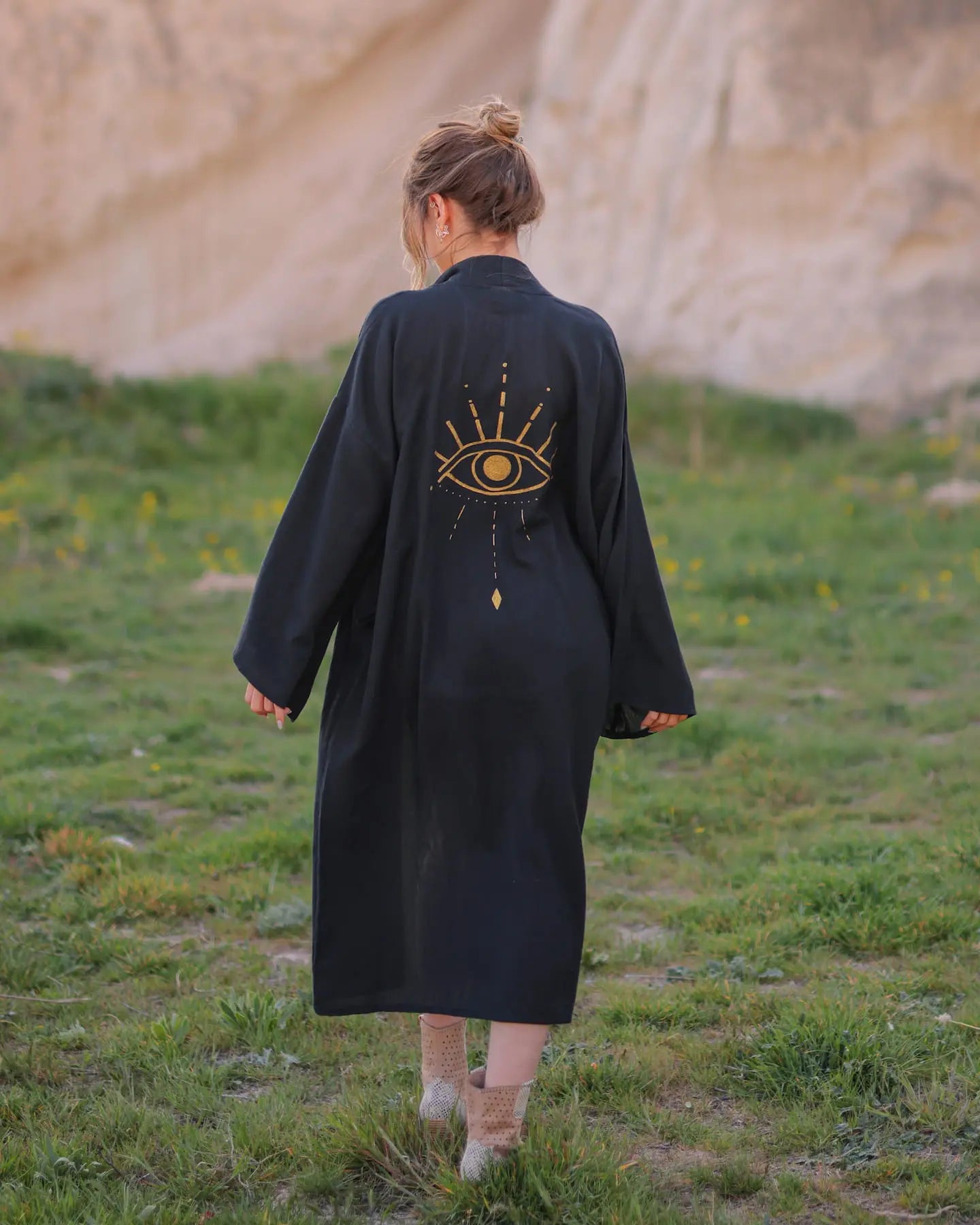 Person wearing a long black robe with a gold evil eye design in a natural setting