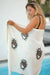 Woman holding a white turkish towel with brown evil eye designs by a pool.