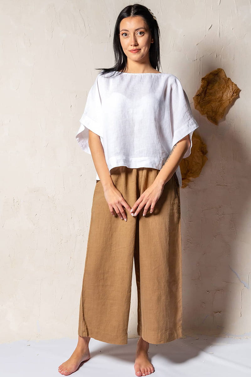 Woman wearing a white top and brown linen palazzo pants against a plain background