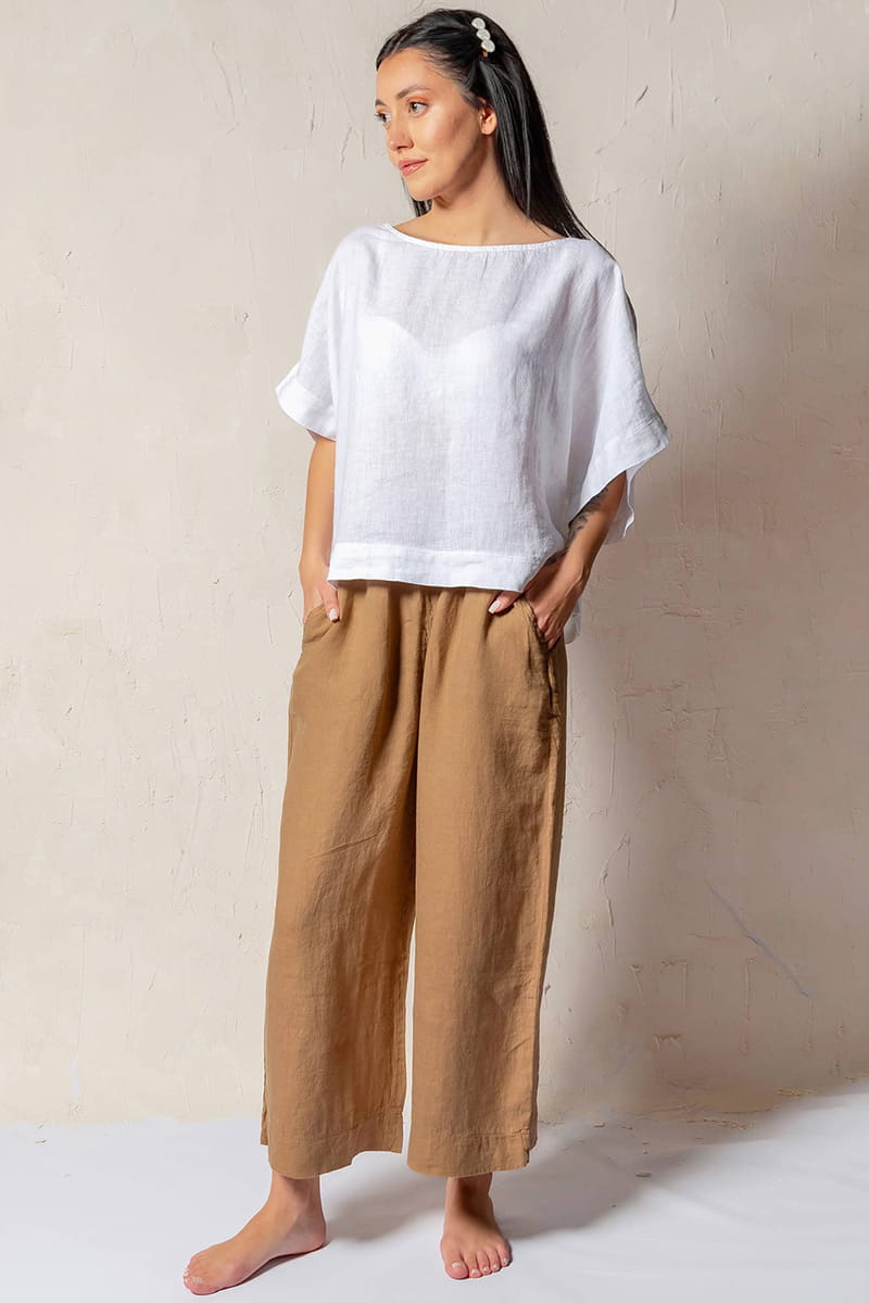 Woman wearing a white top and Brown Linen Pants against a plain background