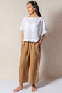 Woman in a white top and brown linen pants against a plain wall — European Flax linen, wide-leg palazzo cut