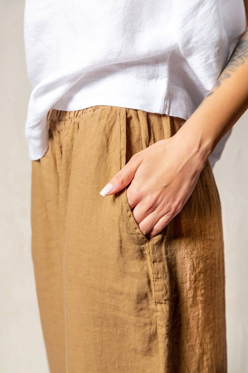 Person wearing a white top and brown linen pants against a neutral background