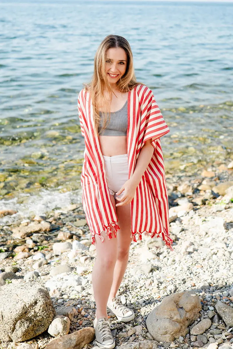 Woman standing on a rocky beach wearing a red and white striped cover-up.
