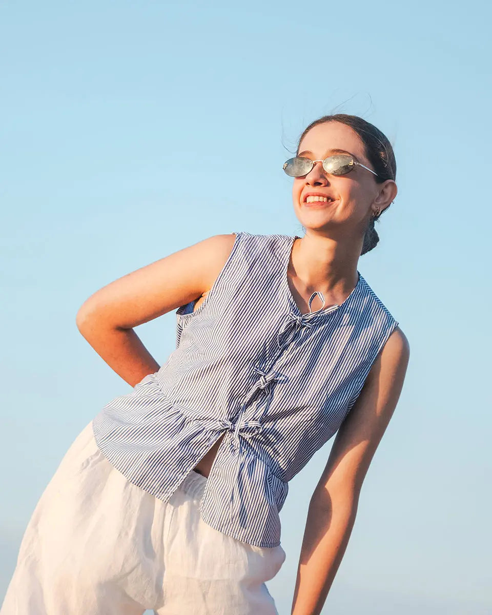 Woman wearing a striped sleeveless Striped top and sunglasses against a clear blue sky.