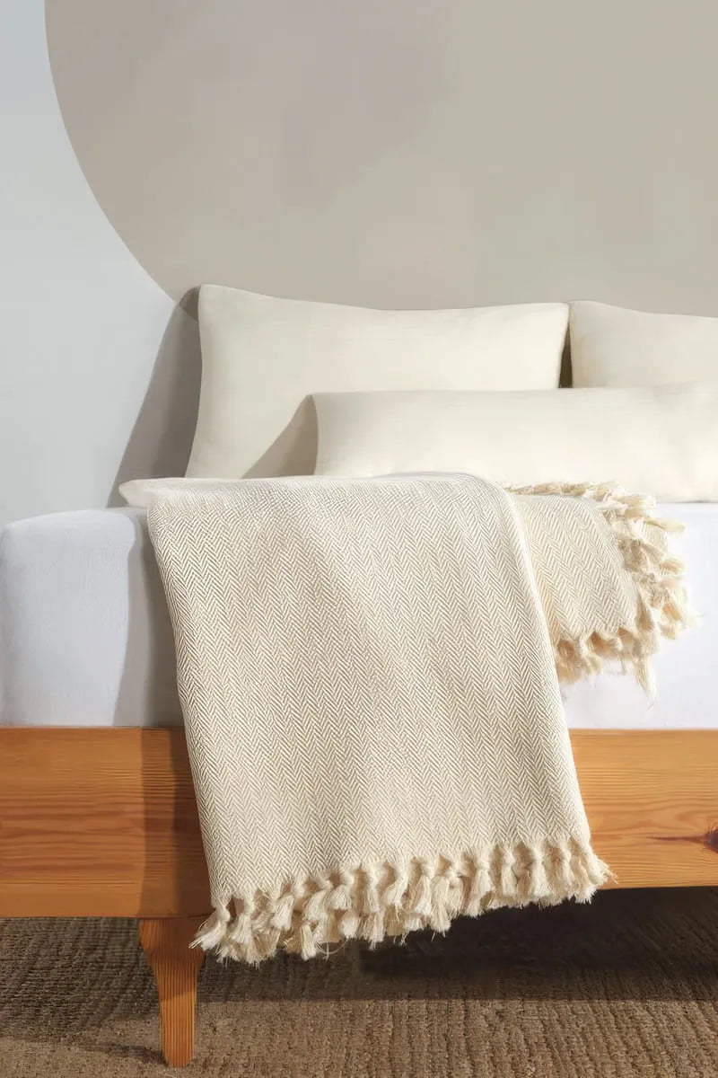 cream blanket with tassels draped over a wooden bed frame.