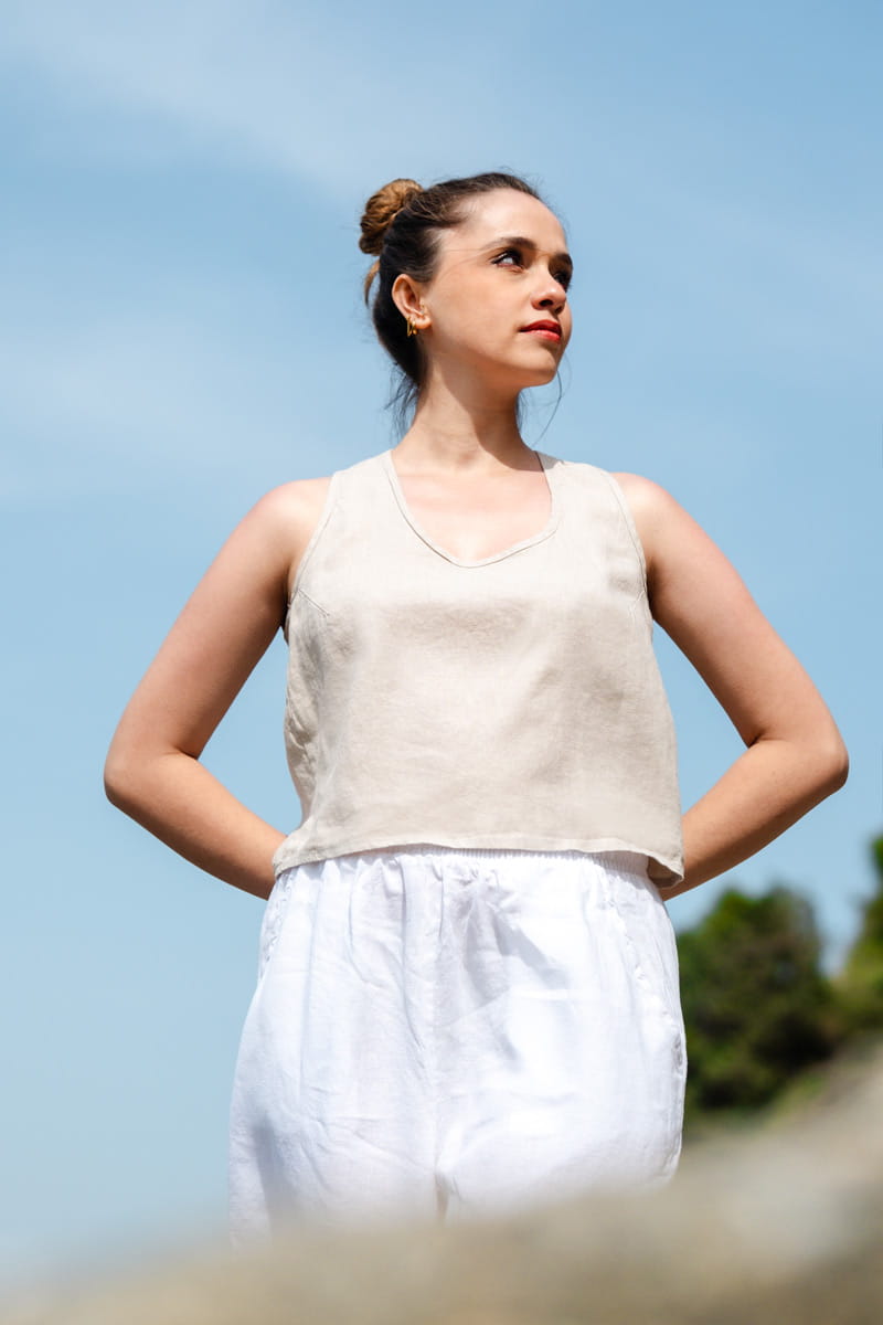 Woman wearing a beige sleeveless top and white pants against a blue sky.