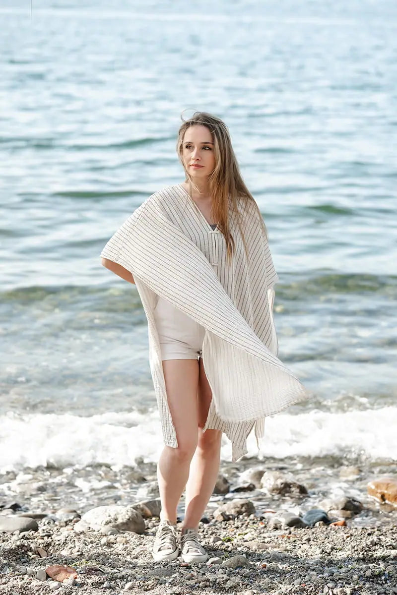 Woman standing on a rocky beach wearing a white poncho.