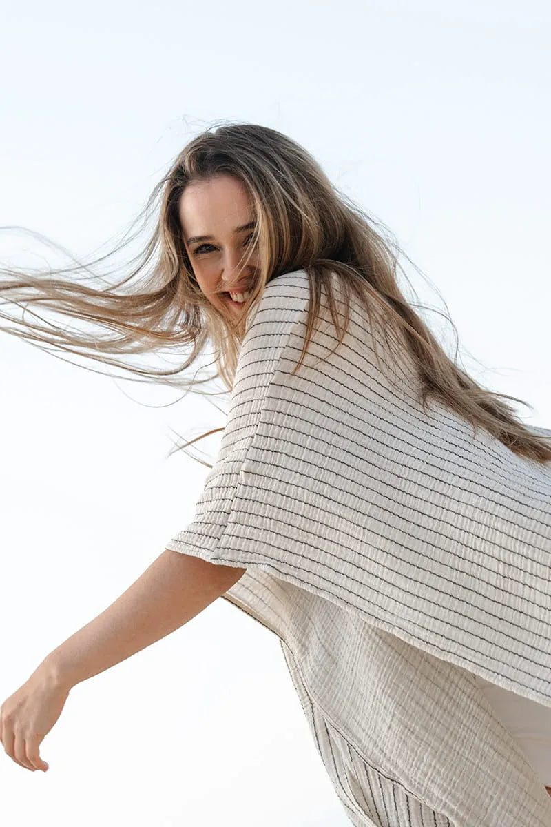 Woman wearing a light-colored cotton swimsuit cover up with flowing hair against a white background