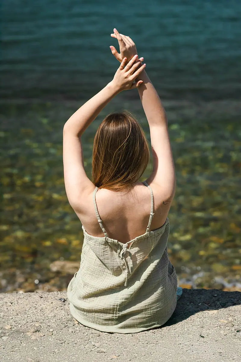 Woman sitting by a body of water with her arms raised