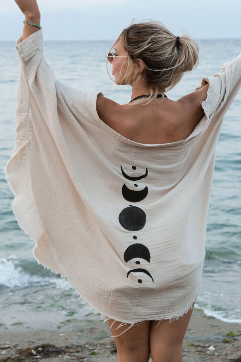 Woman wearing a beige cover-up with black moon phases on a beach
