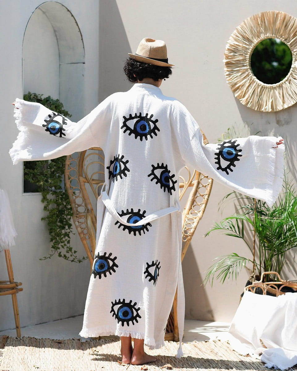 Person wearing a white cover-up with eye patterns in a sunlit outdoor setting.