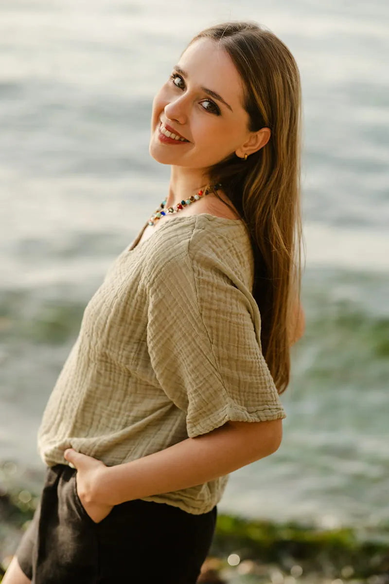 Woman standing by a body of water wearing a green crinkle cotton top.