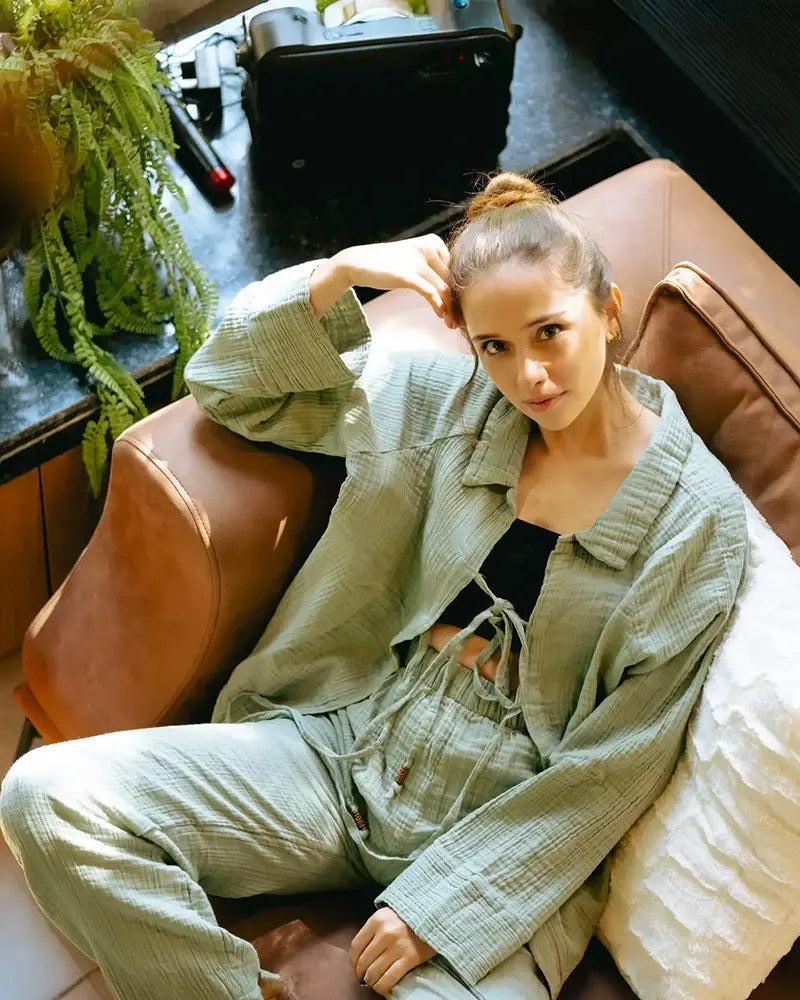 Woman in a green Loungewear Set sitting on a brown couch with a plant in the background