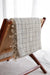 Textured blanket with tassels draped over a wooden chair against a white background
