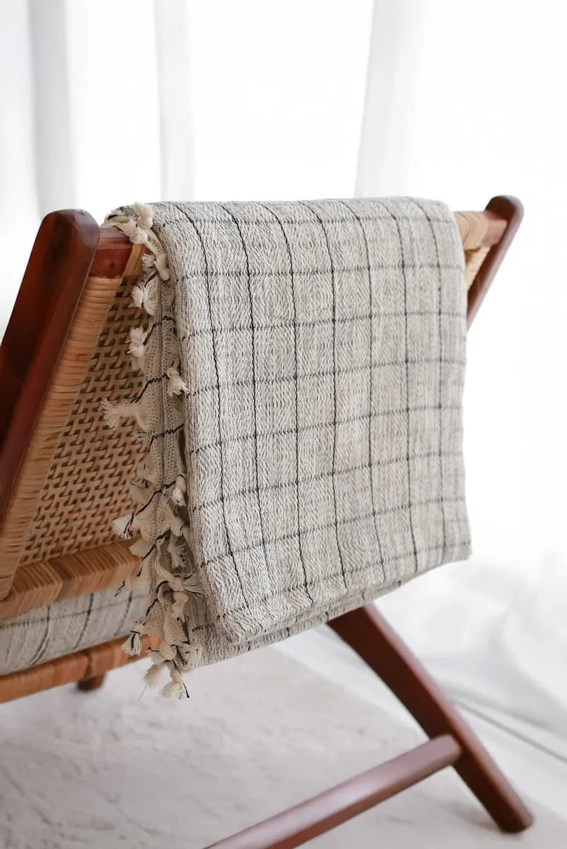Textured blanket with tassels draped over a wooden chair against a white background