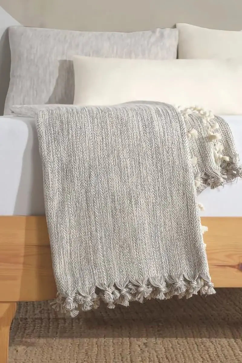 grey cotton bed blanket with pom-poms draped over a bed