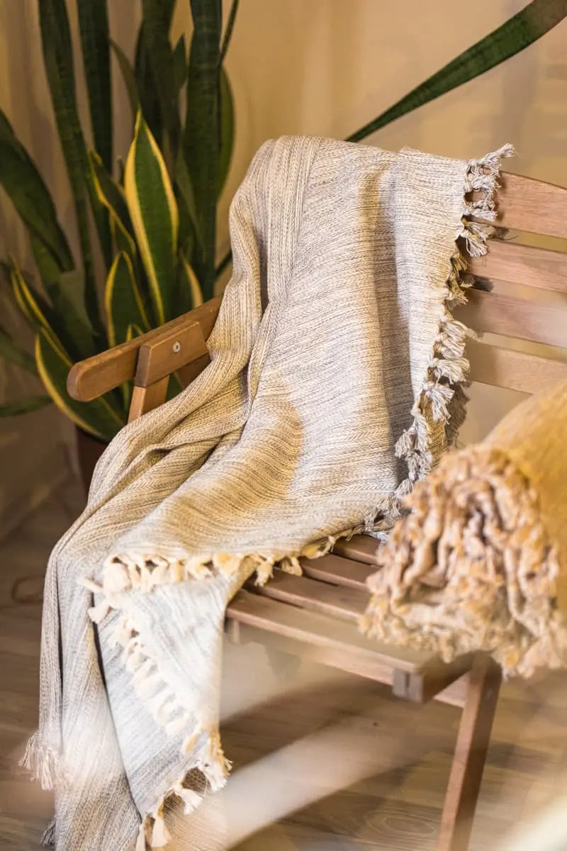 Textured grey blanket draped over a wooden chair with a plant in the background