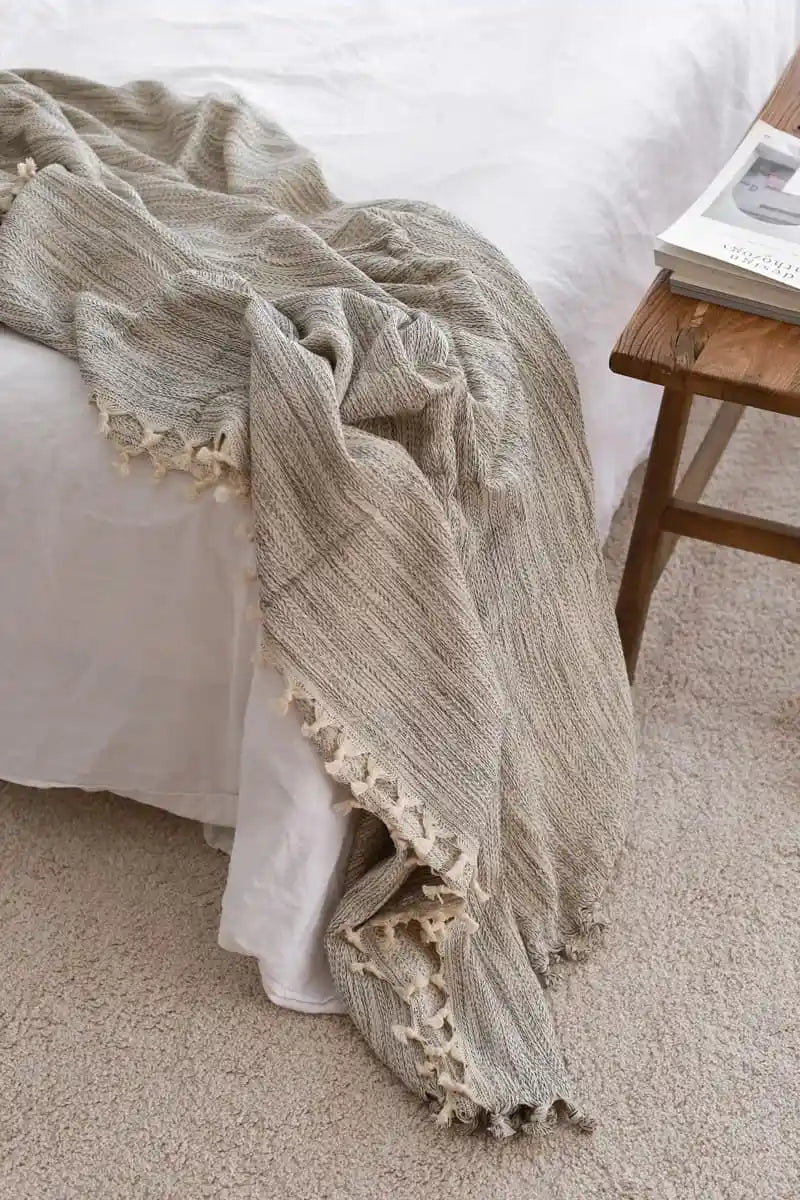 Gray textured  bed blanket with lace trim draped over a bed in a bedroom setting.