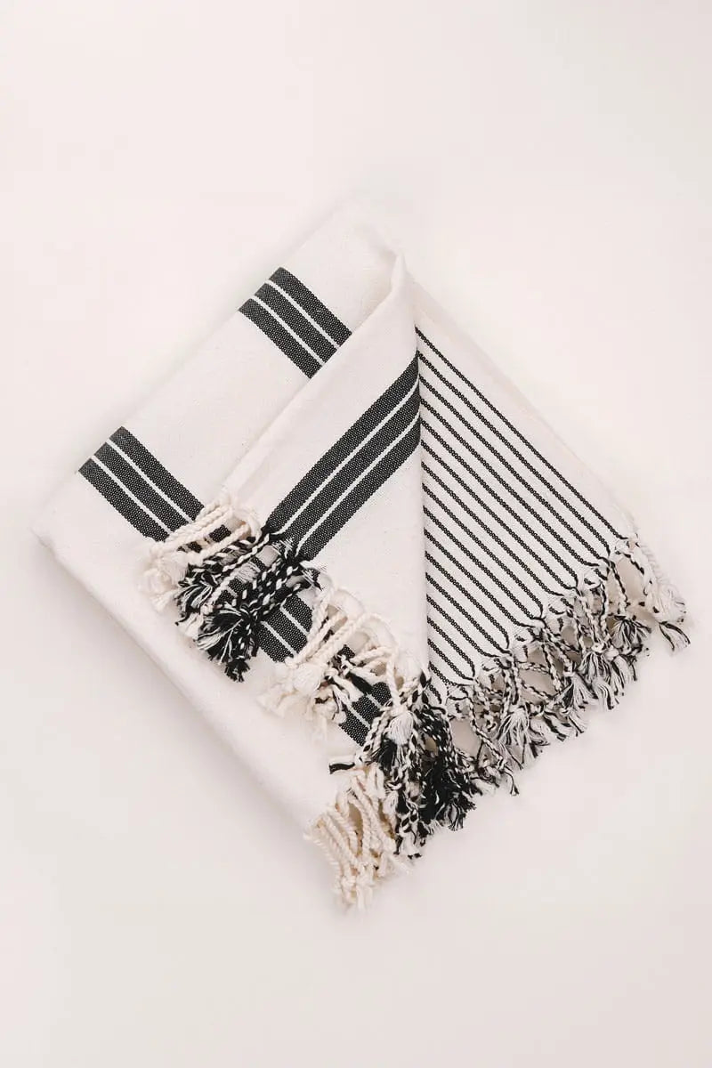 White towel with black stripes and tassels on a light gray background