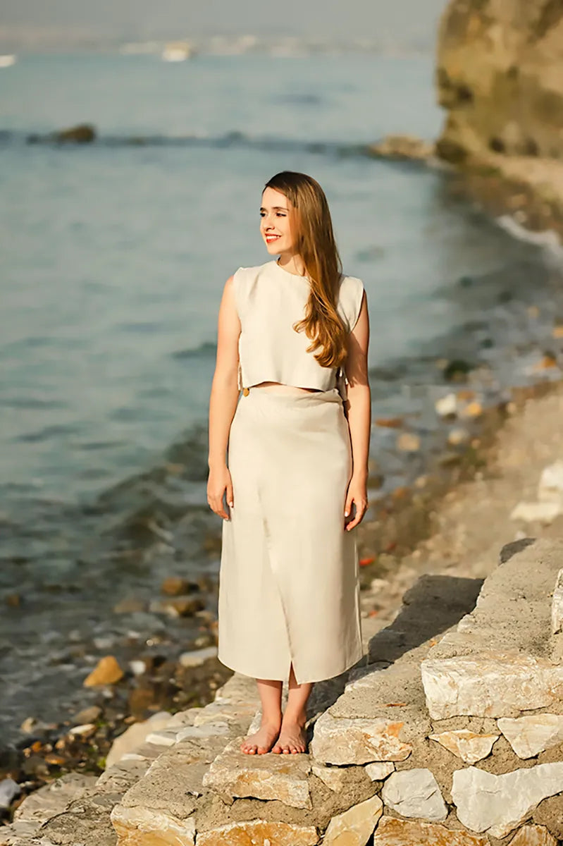 Woman in a linen crop top standing on a stone wall by the sea