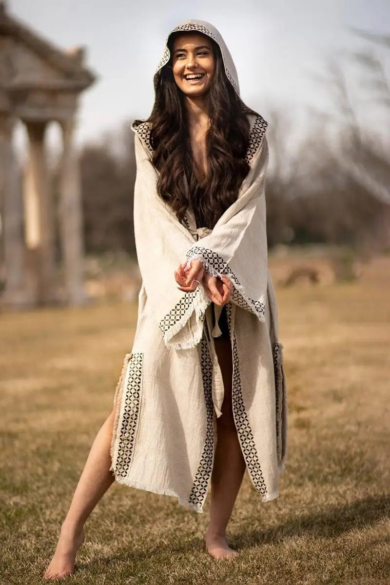 Woman in a long, light-colored linen kimono with a hood standing in an outdoor setting.
