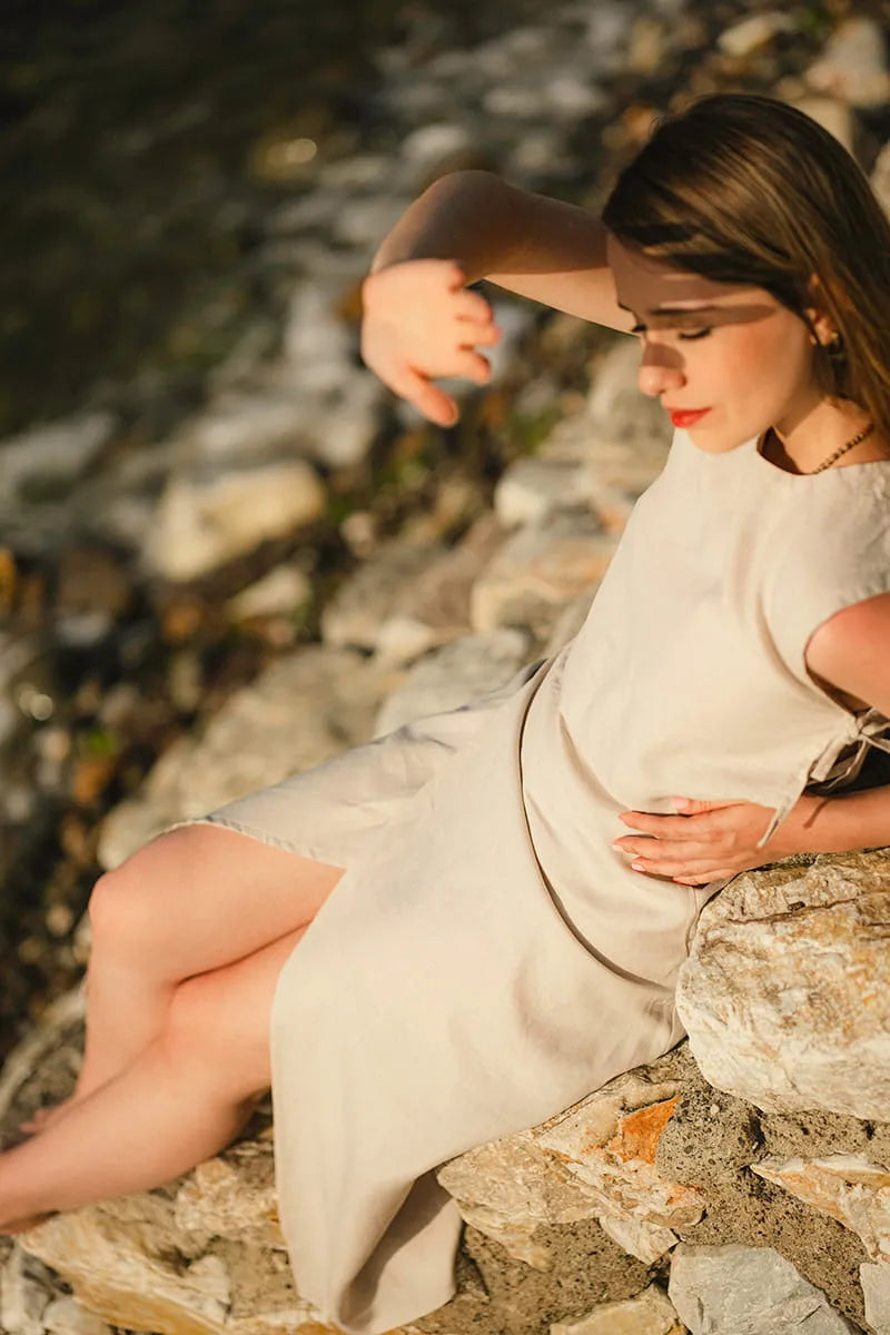Woman in a linen midi skirt sitting on rocks by a body of water