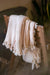cream blanket with tassels draped over a wooden chair in a blurred indoor setting