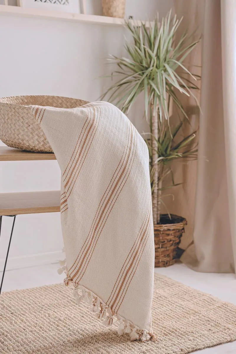 Mustard striped cotton  blanket draped over a chair with a plant and basket in the background