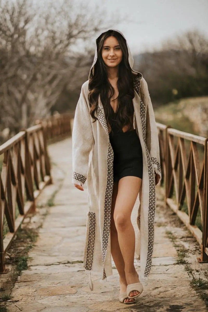 Woman in a long, light-colored robe walking on a wooden bridge with trees in the background