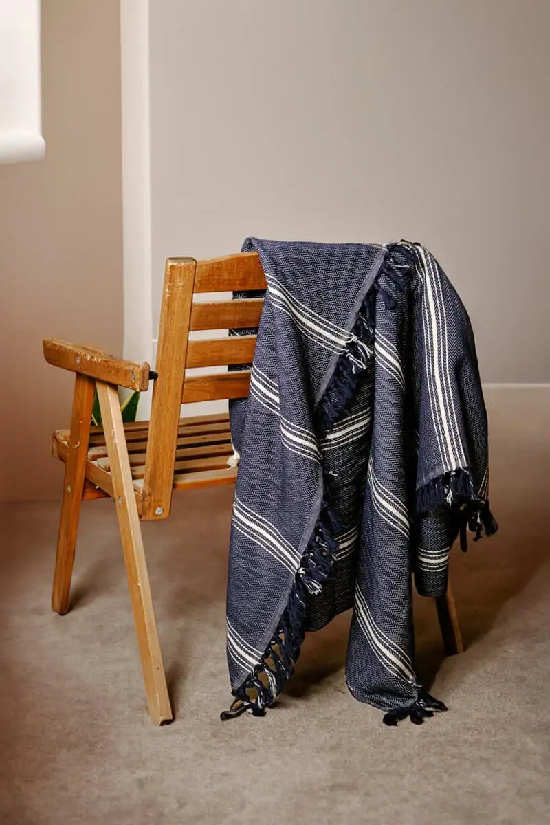 Blue striped towel draped over a wooden chair against a beige wall.