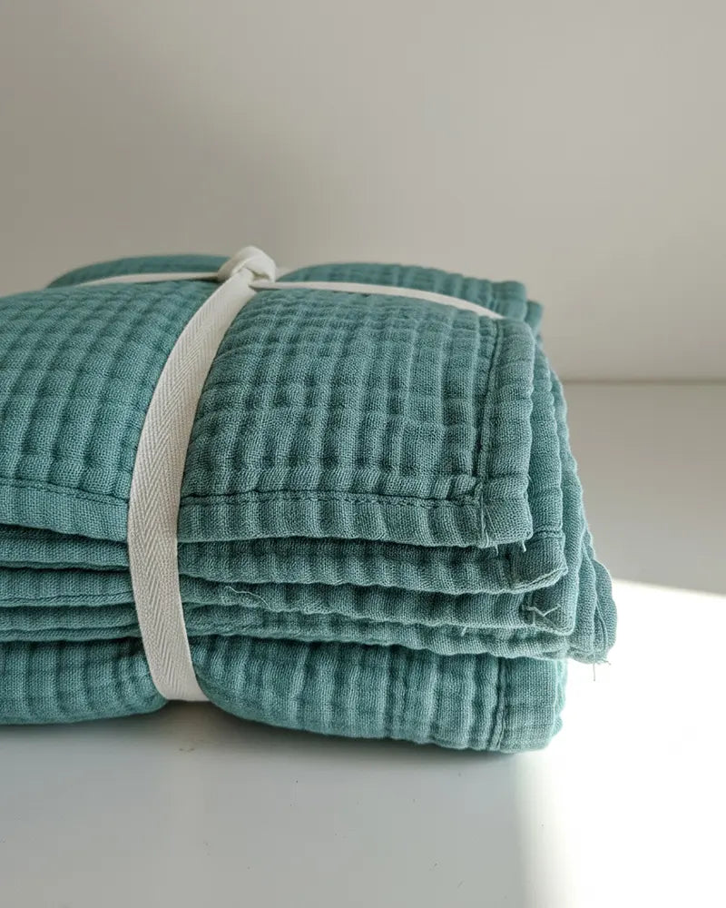 Stack of organic cotton textured towels with white trim on a light surface.