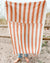 Person standing on a sandy beach with an orange and white striped towel draped over them.