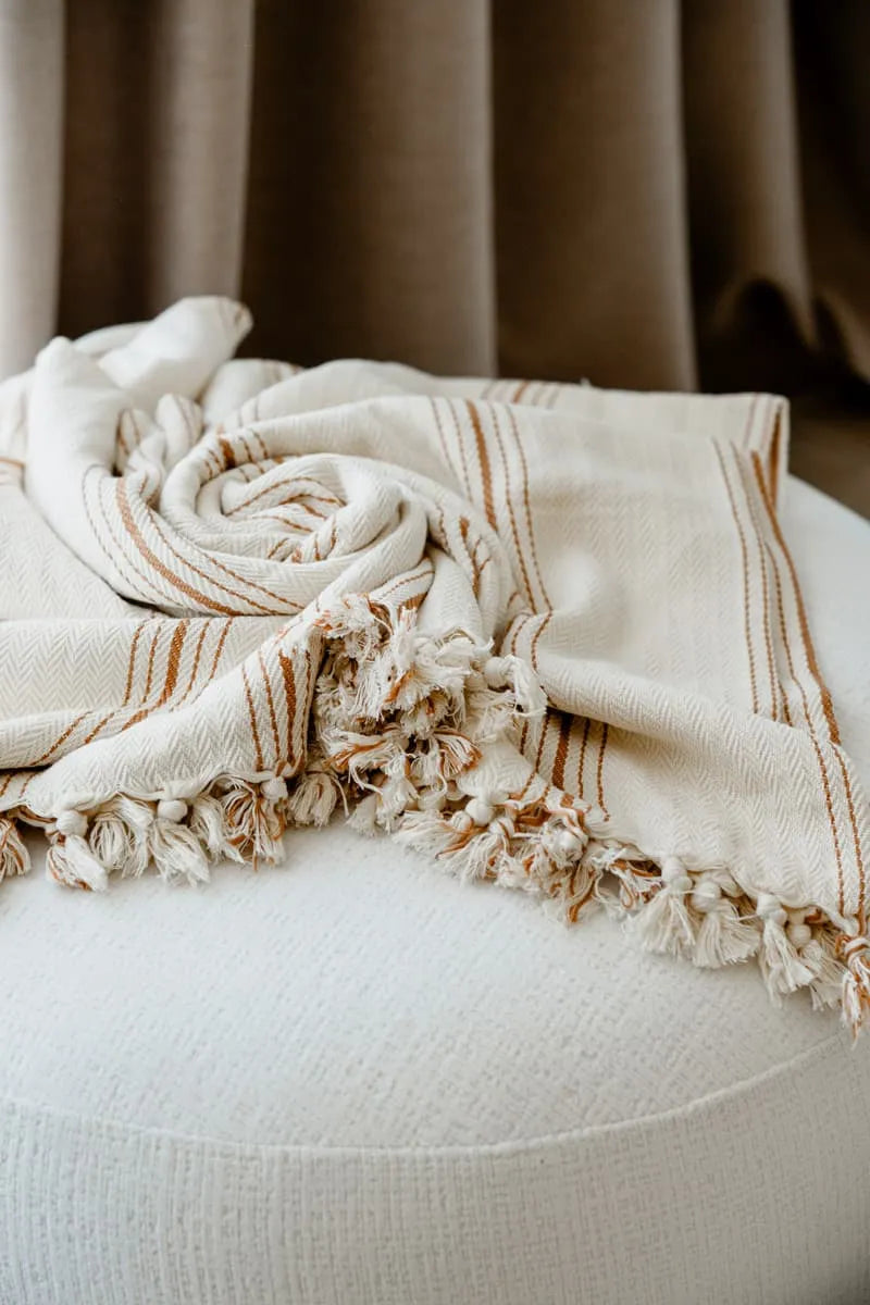 Woven cotton blanket with fringes draped over a white surface