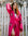 Woman wearing a bright pink robe with eye designs in front of a white picket fence.