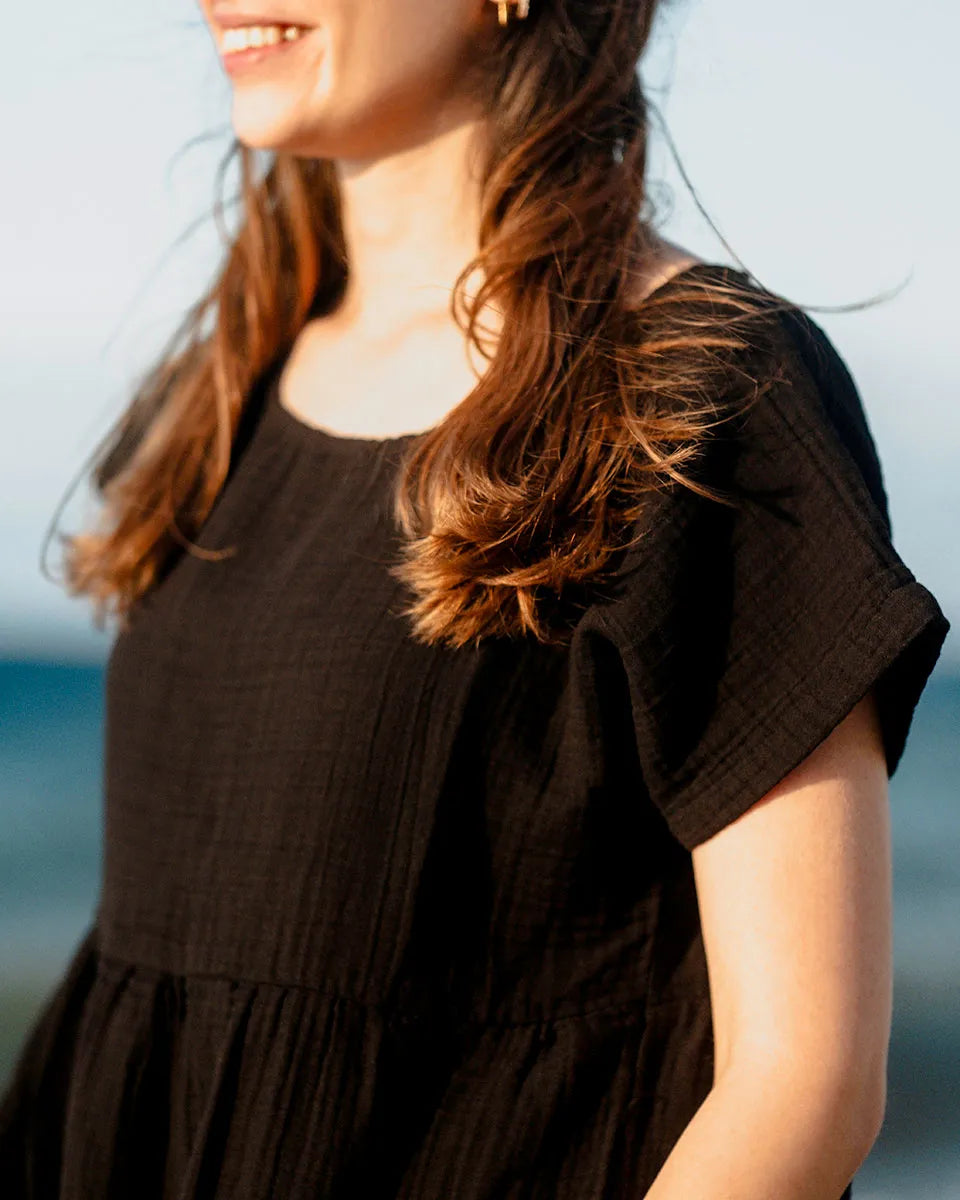 Woman wearing a black short sleeve dress with ruffled sleeves against a blurred natural background