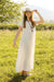 Woman in a white maxi dress and hat standing in a grassy field