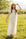 Woman in a white maxi dress and hat standing in a grassy field
