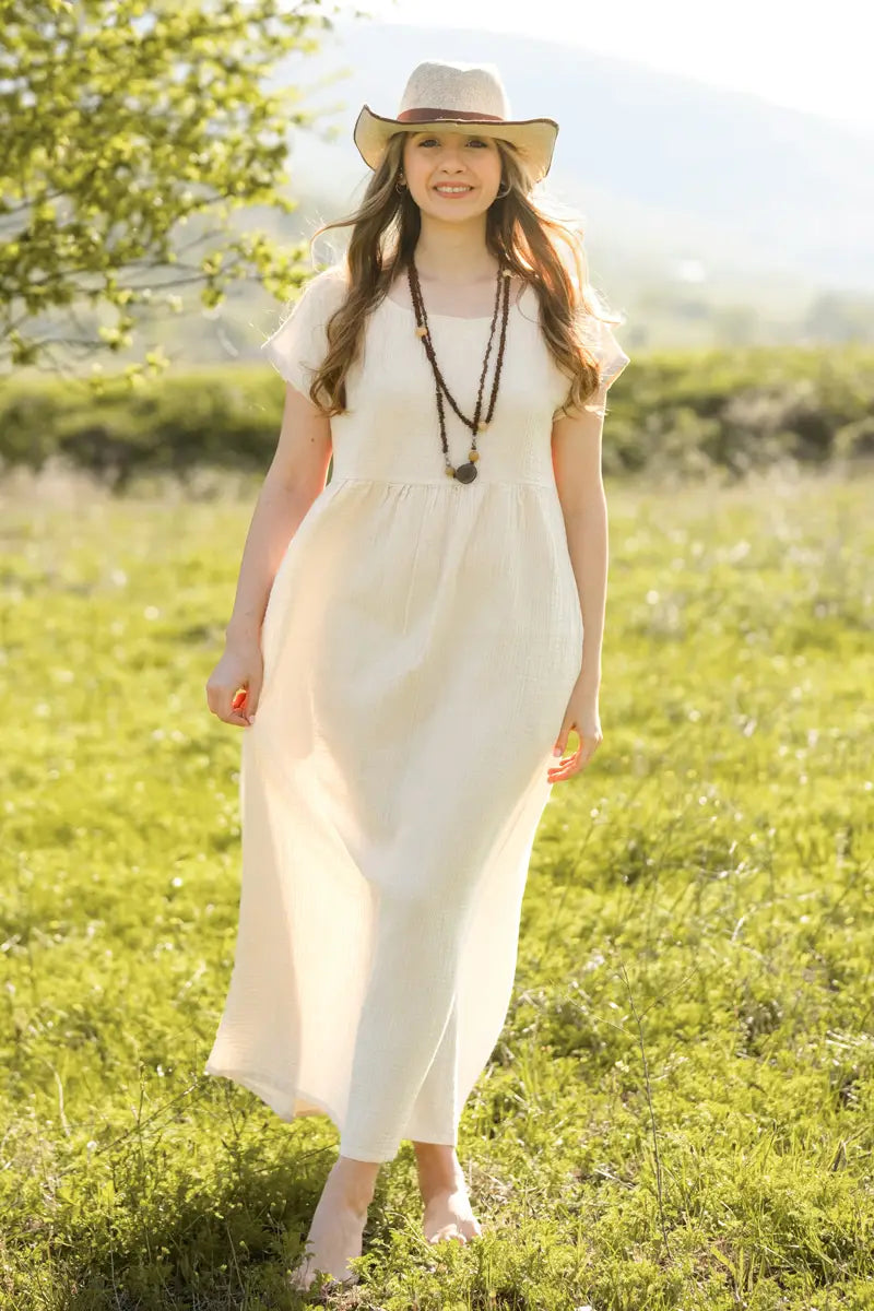 Woman in a white short sleeve dress and hat standing in a grassy field