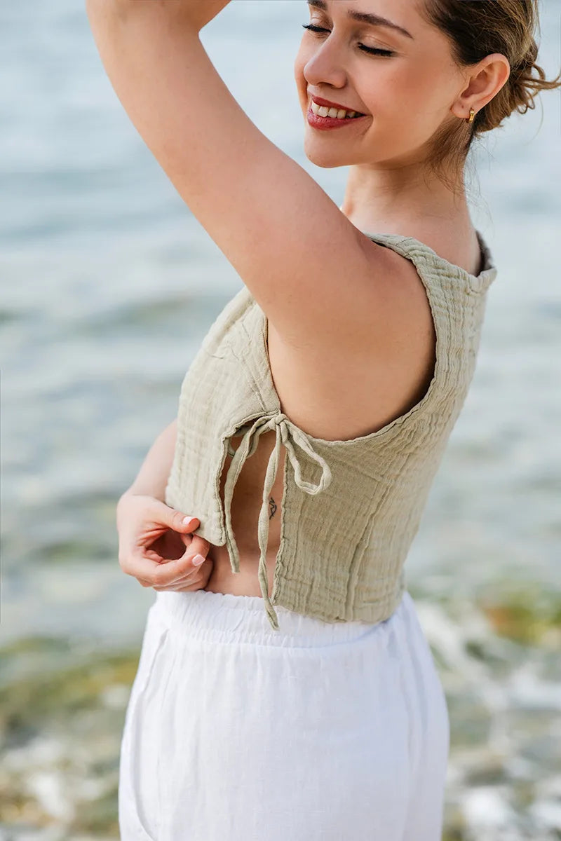 Woman wearing a light green sleeveless top and white pants by a body of water.