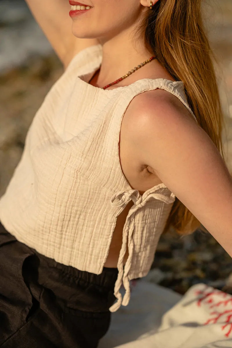 Woman wearing a beige sleeveless top with a blurred natural background