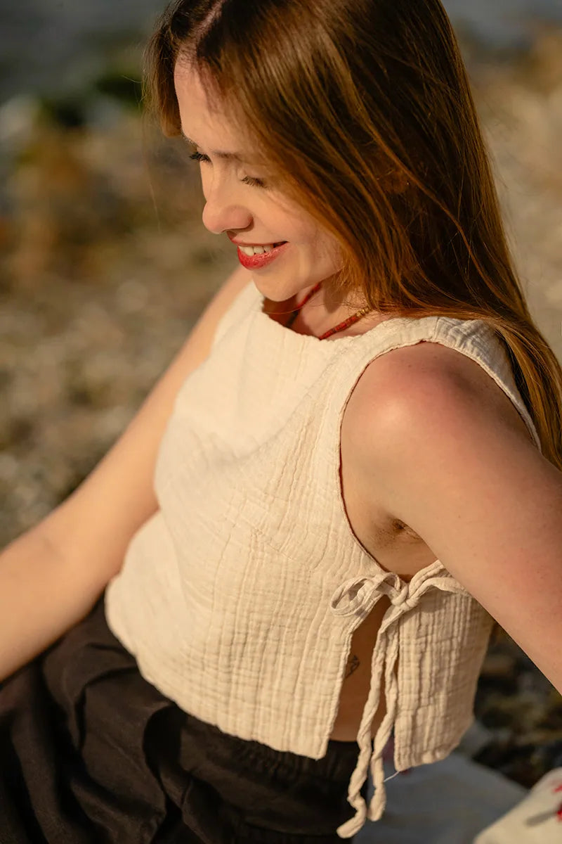 Woman in a beige sleeveless top sitting outdoors with a blurred natural background