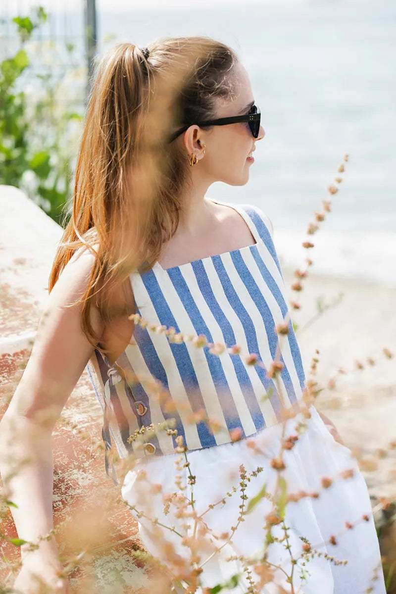 Woman wearing a blue and white striped sleeveless boxy top with a blurred natural background