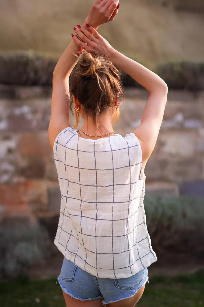 Person wearing a checkered cotton blouse and denim shorts with arms raised outdoors.