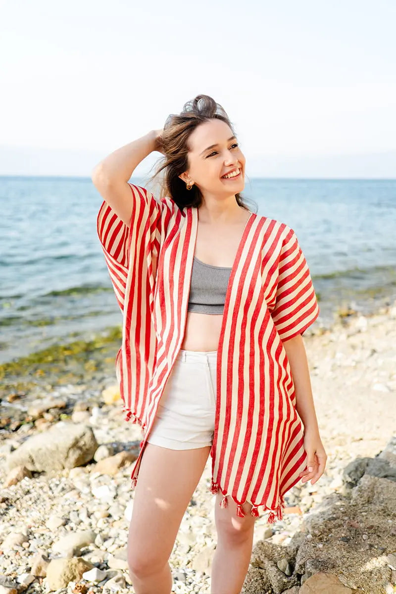 Woman in a red and white striped cover-up standing on a beach.