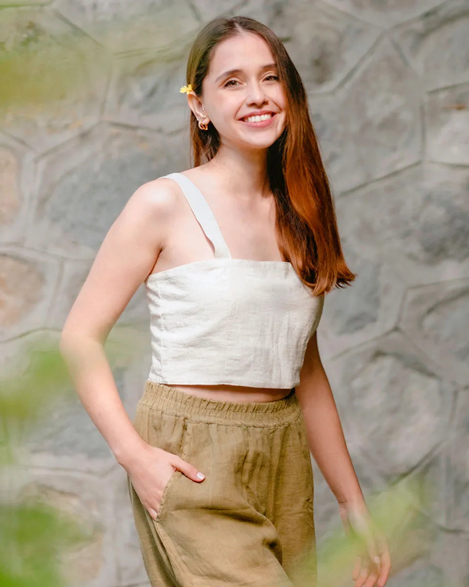 Woman wearing a beige square neck crop top and beige pants against a textured wall.