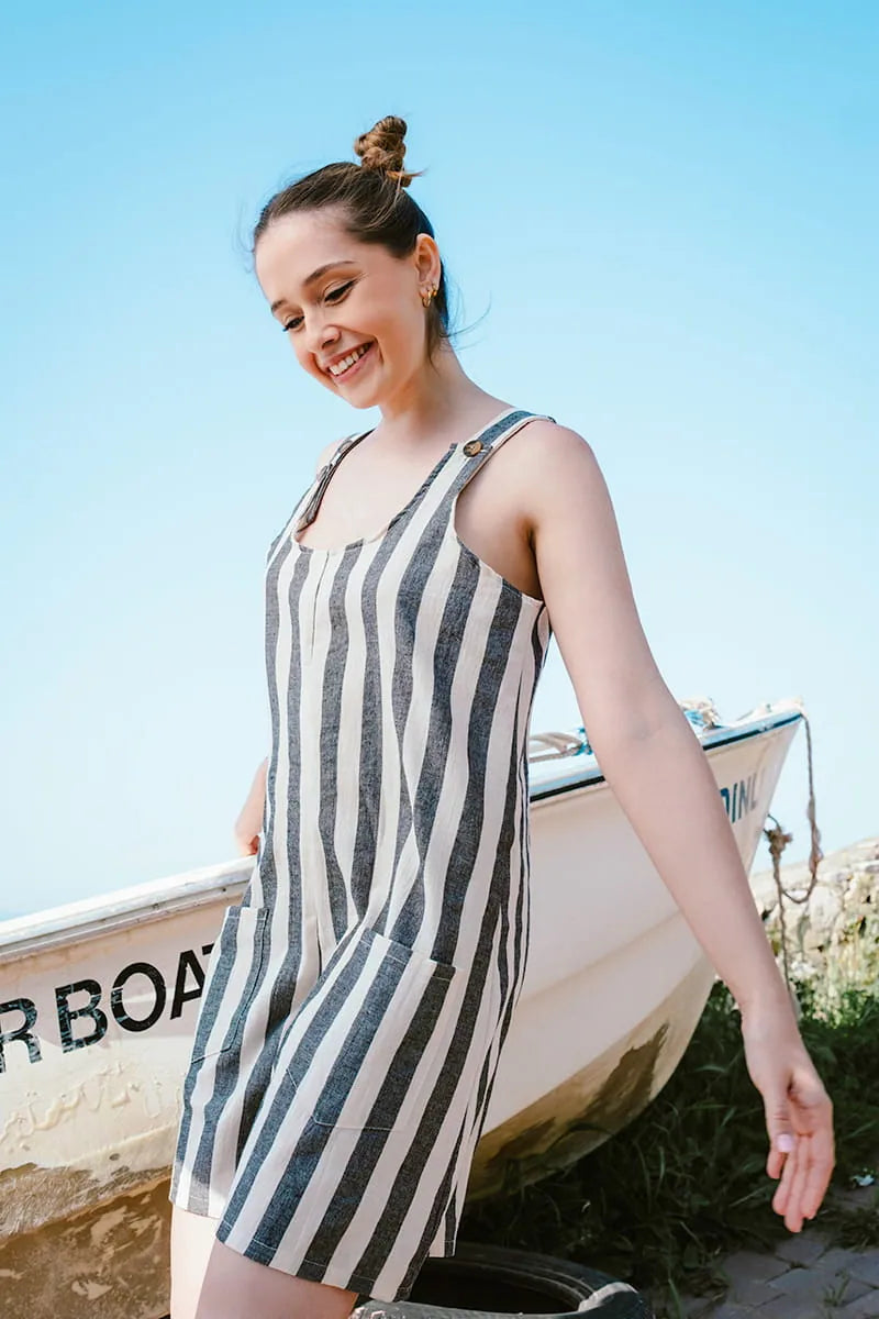 Woman in a striped linen romper standing by a rowboat on a sunny day.