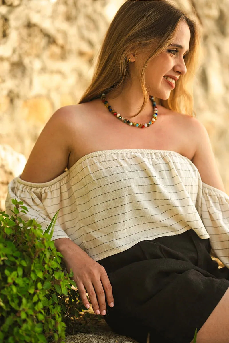 Woman wearing a off-shoulder top and black pants with a blurred natural background