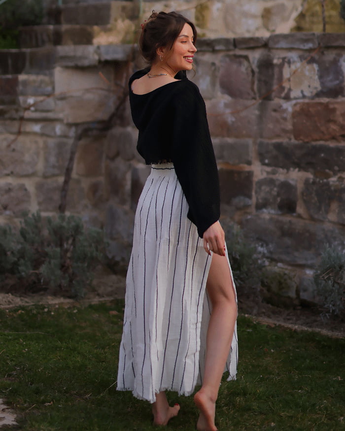 Woman in a black top and striped skirt  standing in front of a stone wall.