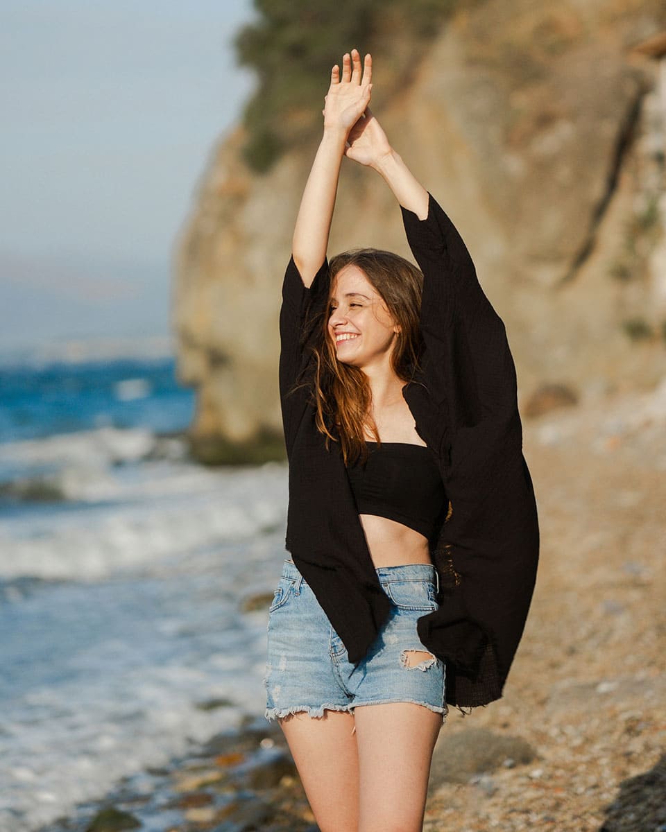 Woman with open front cardigan on a beach with ocean and cliffs in the background